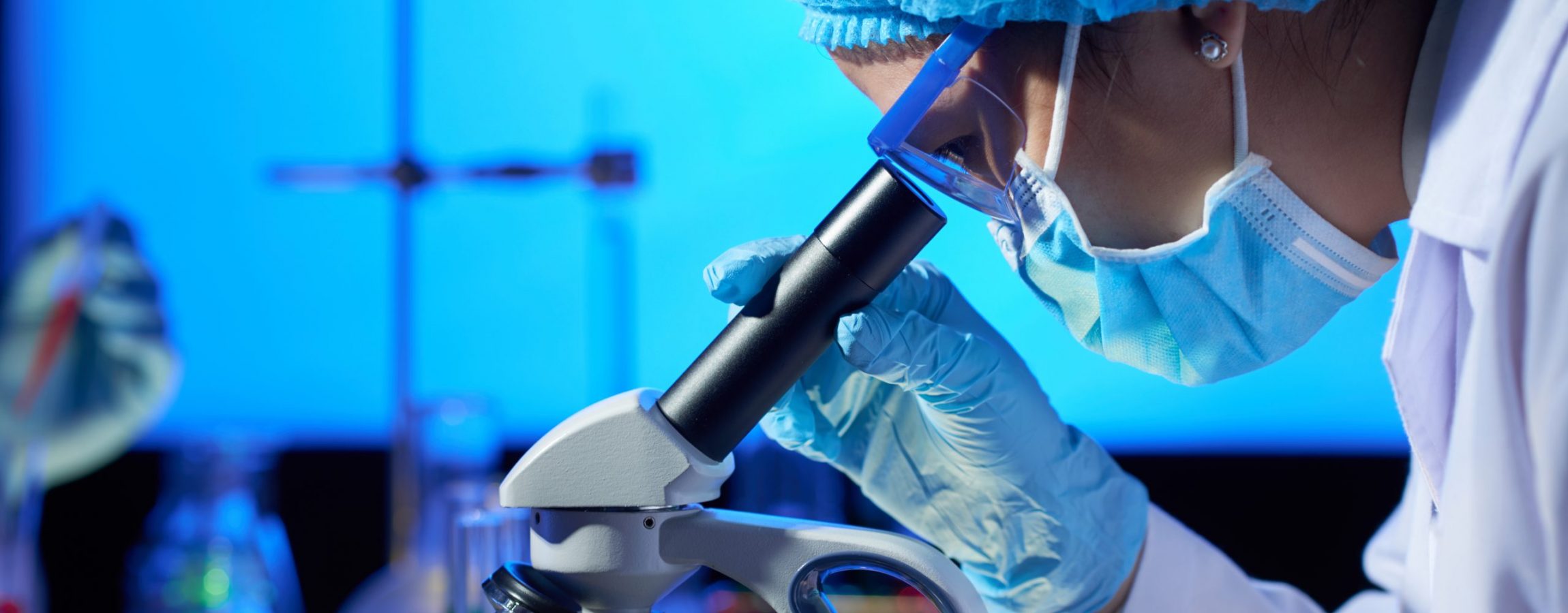 Profile view of concentrated Asian microbiologist examining sample with help of modern microscope while wrapped up in work at dim laboratory
